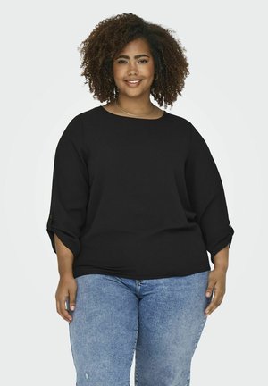 Top negro de manga tres cuartos con cuello redondo y aberturas laterales, combinado con jeans de color azul claro. El material parece suave con una textura lisa.