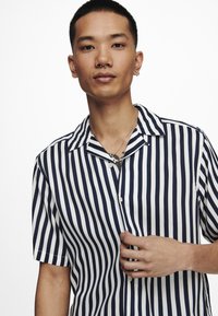 Marineblauw en witte gestreepte korte mouwen shirt met een campkraag, met een knoopsluiting aan de voorkant en een relaxte pasvorm. Gladde stoftextuur.