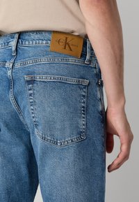 Modre denim hlače s posvetljenim učinkom, z rjavim usnjenim logotipom na pasu in dvema zadnjima žepoma.