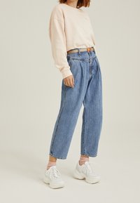 Vaaleanpunainen collegepaita pyöreällä kaula-aukoilla, yhdistettynä väljiin sinisiin farkkuihin. Asusteena on valkoiset lenkkitossut ja vaaleanpunaiset sukat.