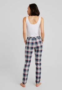 Leichtes, weißes Tanktop kombiniert mit grauen Karohosen, die blaue, rote und schwarze Muster aufweisen. Die Hosen haben einen elastischen Bund.