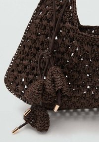Braided brown crochet bag featuring a textured weave, a rounded shape, leather drawstrings with metal accents, and decorative tassels.