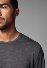 Grå crew-neck t-shirt tillverkad av strukturerad tyg, med subtila horisontella ränder och en avslappnad passform, synlig vid halsringningen och axeln.