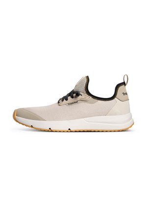Zapatilla deportiva beige y negra con cordones negros, parte superior de malla transpirable, entresuela blanca y suela de goma color marrón claro, mostrada de perfil.