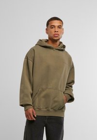 Oliņzaļš filteris ar frontālo kabatu, izgatavots no kokvilnas, pārāk liela izmēra, ar ribotām piedurknēm. Minimālas logo detaļas uz krūtīm.