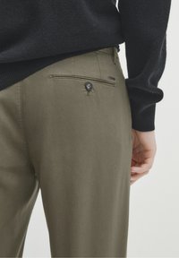 Pantaloni khaki con una superficie liscia, dotati di una tasca posteriore con chiusura a bottone e un discreto etichetta del marchio vicino alla vita.
