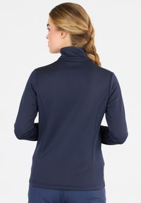 Marinblå zip-up jacka med hög krage, texturerad herringbone-mönster och figursydd design med långa ärmar. Bakifrån visas.