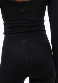 Κοντινό πλάνο ενός ατόμου που φοράει μαύρο αθλητικό τοπ και κολάν Nike με εμφανή λογότυπα Nike στη μέση και στο πάνω μέρος της πλάτης.