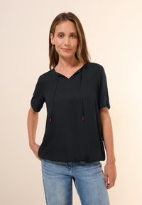 Kortærmet sort hoodie med v-hals, lavet af tekstureret stof. Har justerbare snore med lilla spidser og en afslappet pasform.