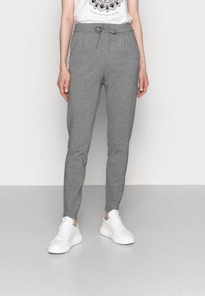 Person wearing gray drawstring sweatpants, white sneakers, and a white t-shirt with a black mandala design and text.