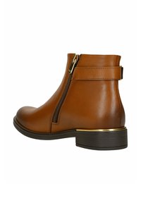 Braune Leder-Stiefelette mit seitlichem Reißverschluss, Riemenakzenten, niedrigem Blockabsatz und dünnem goldenen Trim über der Sohle.