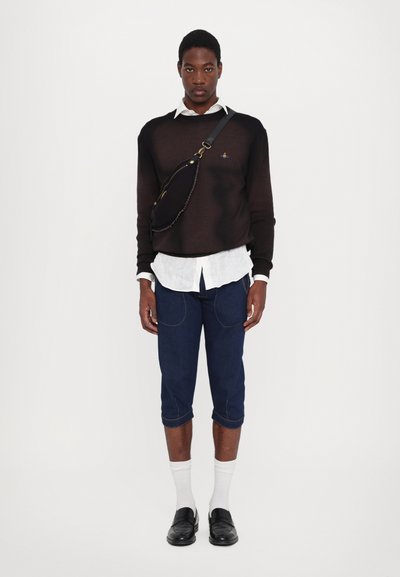 Pull en tricot noir superposé sur une chemise blanche à boutons ; jean cropped bleu marine avec des coutures visibles ; sac à épaule ; mocassins noirs ; chaussettes blanches.