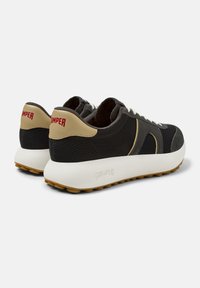 Czarne siateczkowe sneakersy z beżowymi akcentami i białą podeszwą. Mają zaokrąglony kształt, sznurówki oraz czerwone logo na pięcie. Fakturowane powierzchnie.
