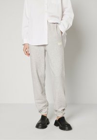 Pantalons de survêtement gris en tissu doux, avec des poignets élastiques et un logo vintage imprimé sur le côté gauche, associés à des sabots noirs.