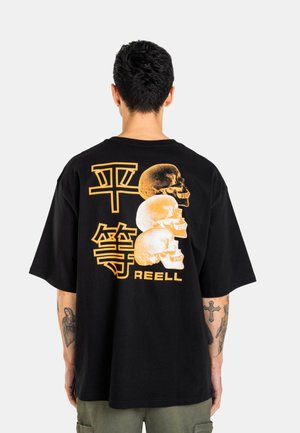 Mann mit kurzen dunklen Haaren steht mit dem Rücken zur Kamera und trägt ein schwarzes T-Shirt mit drei gelben Totenköpfen und japanischen Schriftzeichen auf dem Rücken.
