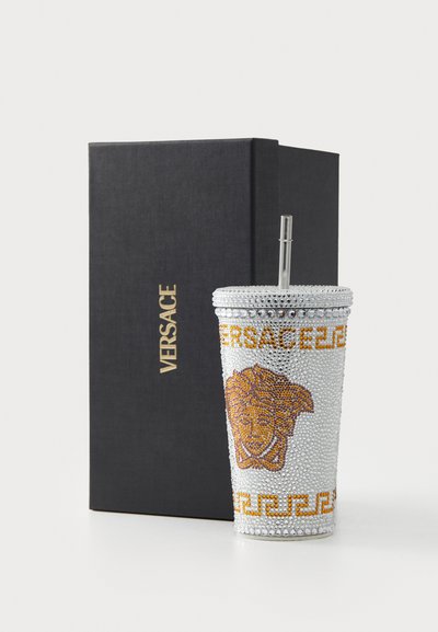 Zigantni vodeni tumbler s srebrnim rhinestones, narančastim grbom lava i zlatnim tekstom "VERSACE", uz crnu pravokutnu kutiju.