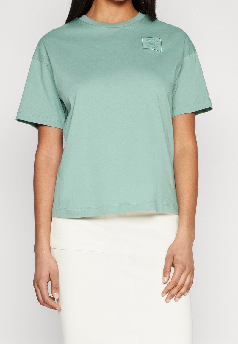 Mátově zelené tričko s krátkým rukávem vyrobené z bavlněné tkaniny. Obsahuje čtvercovou nášivku s logem na levé hrudi. Design rovného lemu s uvolněným střihem.