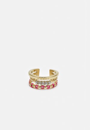 Åben ring i guld-tone med GUESS-logo, fem klare krystaller og en pink og gylden kædedetalje.