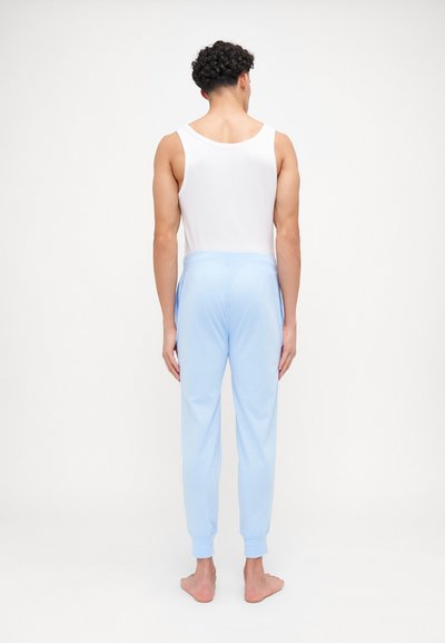 Lys blå joggebukser med elastisk liv og mansjetter, parret med en hvit singlet, sett bakfra. Myk stofftekstur.