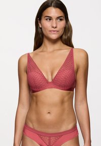 Sujetador de encaje color rosa con diseño de escote en V profundo y tirantes anchos; combinado con unas braguitas a juego que presentan un patrón de encaje similar.