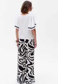 Biała bluzka z czarnym falbankowym wykończeniem, w połączeniu z szerokimi spodniami o odważnym czarno-białym abstrakcyjnym wzorze. Gładka tekstura materiału.