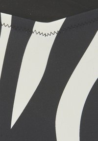 Čierno-biely vzorovaný textil so hladkou štruktúrou. Obsahuje odvážne, zvlnené vzory v kontrastných farbách. Upravené švy pozdĺž okrajov.