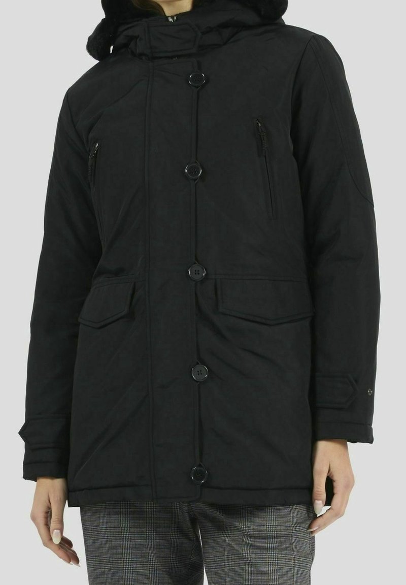 Svart, knäppt vinterjacka med framfickor och blixtlåsfickor på bröstet, bärs över rutiga byxor.