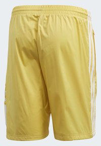 Gula badbyxor med en slät textur, elastisk midja och vita sidostråk. Inkluderar en säker ficka på vänster sida.