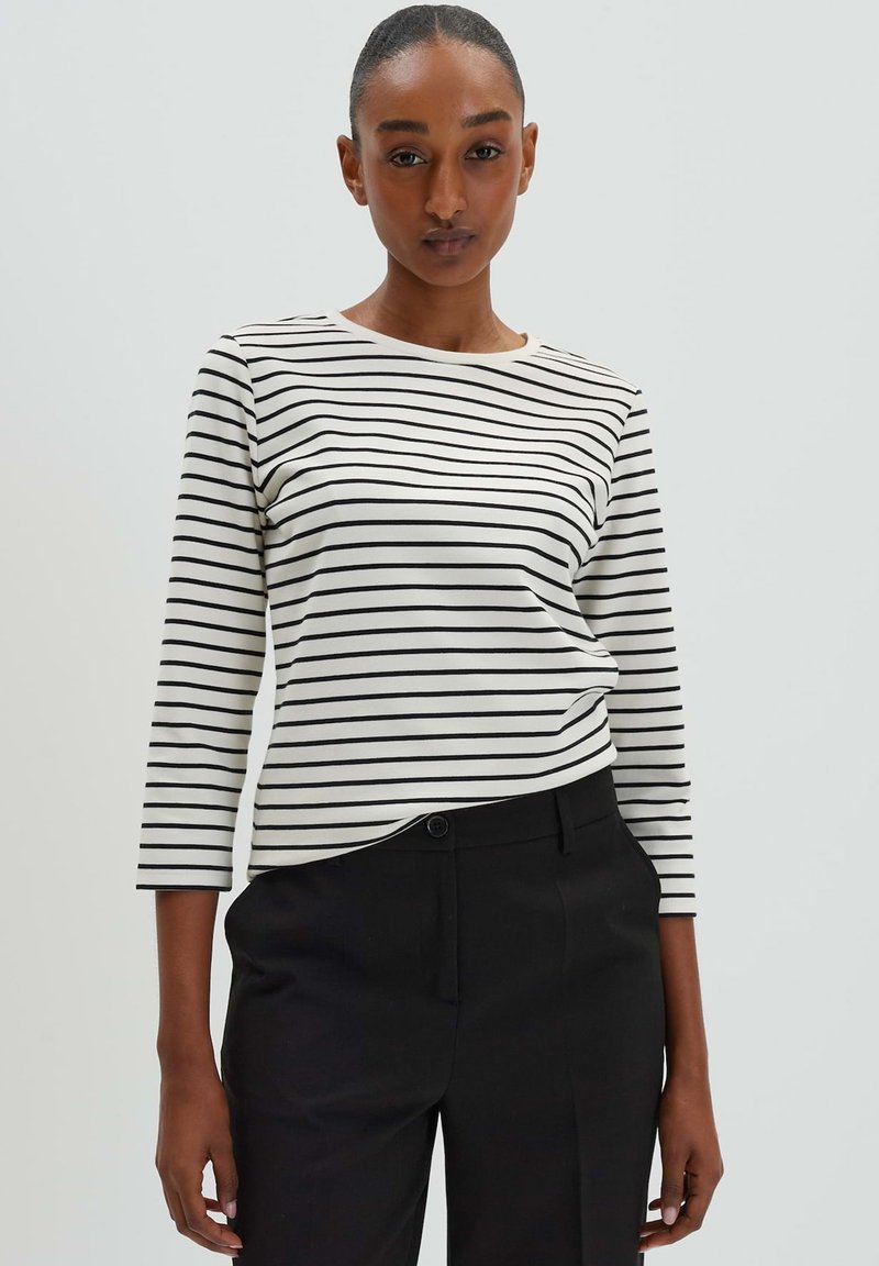 Camicia a maniche lunghe a righe con righe orizzontali nere e bianche, scollo rotondo e tessuto morbido. Indossata con pantaloni neri su misura.