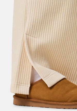 Cremefarvet ribbet stof med en sideslids, parret med en brun ruskindsslipper med en tekstureret sål og kontrasterende pynt.