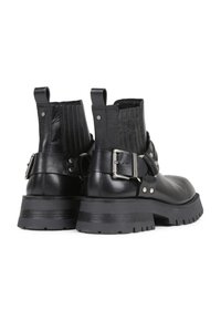 Botas de tobillo de cuero negro con un respaldo texturizado, detalle de hebilla y suela gruesa. Cuenta con herrajes plateados y paneles laterales elásticos.