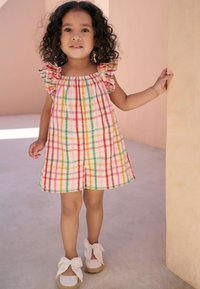 Checked cotton dress in pink with red, yellow, and green stripes; features ruffled sleeves. White espadrille shoes with bow accents.