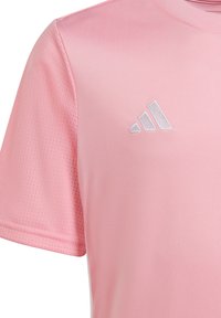 Lichtroze sportshirt gemaakt van soepel materiaal met een ademende textuur. Heeft een wit Adidas-logo aan de bovenkant van de linkerzijde.