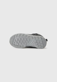 Suela de una zapatilla deportiva negra con una banda de rodadura de goma gris que presenta patrones de diamantes y líneas sobre un fondo blanco.