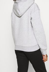 Sudadera gris con capucha, de corte relajado, con puños y dobladillo acanalados, que presenta una textura suave y un diseño simple. La vista trasera muestra la capucha y las costuras.