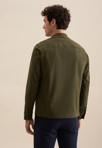 Olivgrüne Jacke mit strukturiertem Design, langen Ärmeln und knopfförmigen Manschetten. Glatte Textur, minimalistischer Rücken mit einem subtilen Passe-Detail.