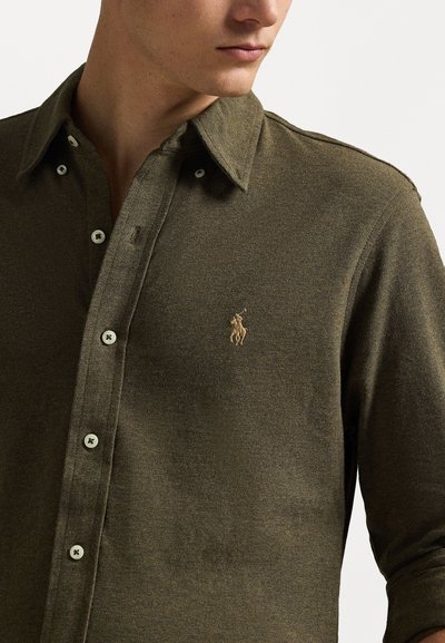 Camicia verde oliva con bottoni in un tessuto testurizzato, dotata di colletto classico, bottoni bianchi e un piccolo logo ricamato sul petto.