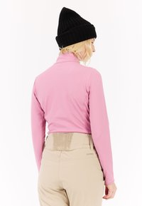 Šviesiai rožinė, ilgomis rankovėmis bluzonė su apykakle, derinama su smėliniais kelnais, turinčiais tekstūruotą juosmenį ir logotipą. Juodas megztas kepurė.