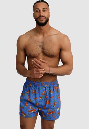 Blaue Badeshorts mit einem elastischen Bund, ausgestattet mit einem orangefarbenen Tiger- und Pflanzenmuster. Leichter Stoff mit einer lockeren Passform.