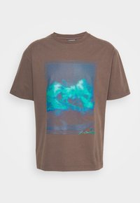 Brązowa bawełniana koszulka z grafiką przedstawiającą turkusowe i niebieskie górskie krajobrazy na przodzie oraz okrągłym dekoltem i krótkimi rękawami.