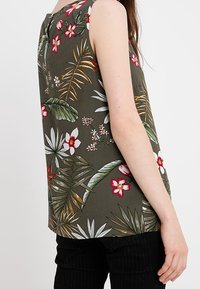Bezramkowy top w ciemnozielonym materiale z kwiatowym wzorem w czerwone i białe kwiaty oraz zielone liście. Prosty krój i luźny fason.