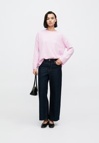 Ροζ πλεκτό τοπ με μακριά μανίκια, σκούρο μπλε τζιν με φαρδιά πόδια, μαύρες μπαλαρίνες και μια μικρή μαύρη τσάντα χειρός, όλα τοποθετημένα σε απλό λευκό φόντο.