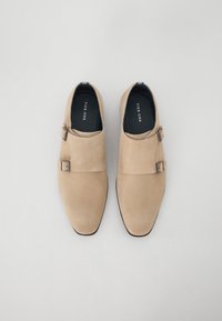 Beige Wildlederschuhe mit doppeltem Schnallen-Design, spitzem Zehenbereich und flacher Sohle. Das Innere ist mit einem schwarzen Futter und Markenlogo ausgestattet.