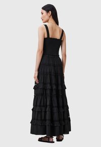 Robe maxi noire avec un buste smocké, larges bretelles et un design à volants superposés. Fabriquée en tissu léger, avec de délicates accents en dentelle.