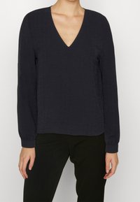 Ciemnoniebieski długi rękaw z dekoltem w serek, teksturowana tkanina i elastyczne mankiety, w połączeniu z czarnymi spodniami.