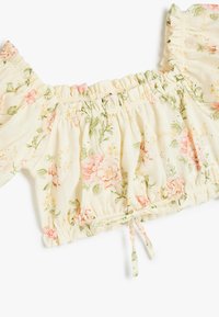 Blomstret crop top i let, elfenbenfarvet stof. Har rynkede ærmer, samlet elastisk talje og et pink og grønt blomstermønster.