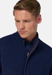 Marineblauer Reißverschluss-Pullover aus weichem Stoff mit hohem Kragen und kontrastierendem blauen Innenfutter. Verfügt über dezente Nähte und einen silbernen Reißverschluss.