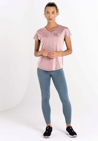 Camiseta deportiva de manga corta color rosa claro con escote en V y textura sutil, combinada con leggings ceñidos color teal y zapatillas deportivas negras.