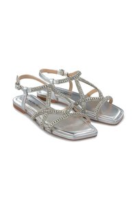 Srebrne płaskie sandały z krzyżującymi się paskami ozdobionymi cyrkoniami, kwadratowym noskiem i regulowanym paskiem na kostkę.