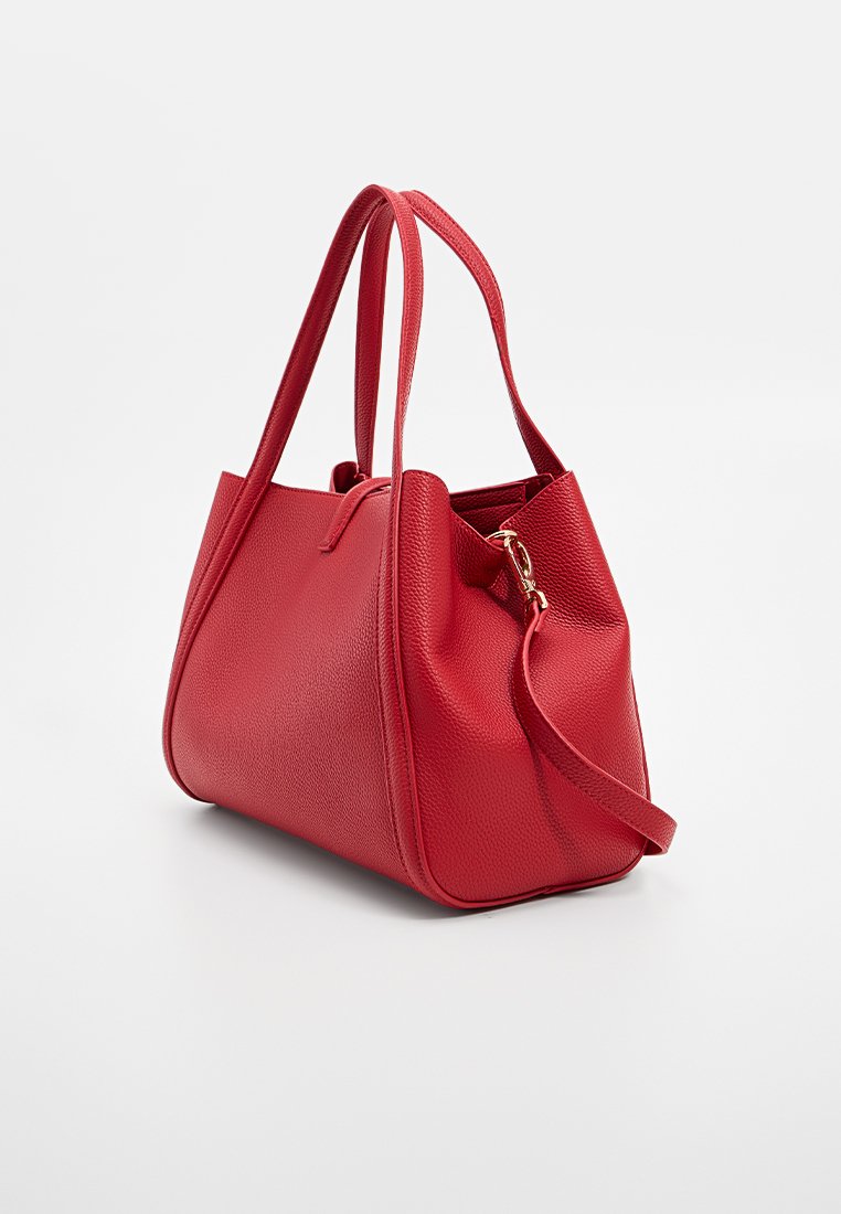 Sac à main en cuir rouge texturé avec deux poignées supérieures et une bandoulière amovible, incliné pour montrer les détails de côté et de l'avant.